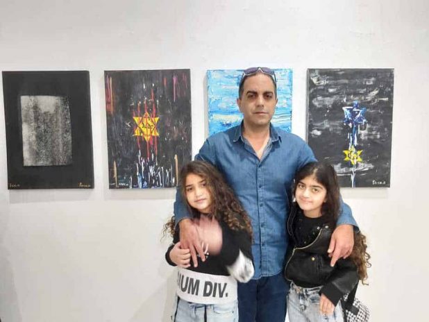 אייל מויאל עם הבנות דניאל ועדן. ברקע עבודותיו מסדרת "עפר ואפר" | צילום: עצמי